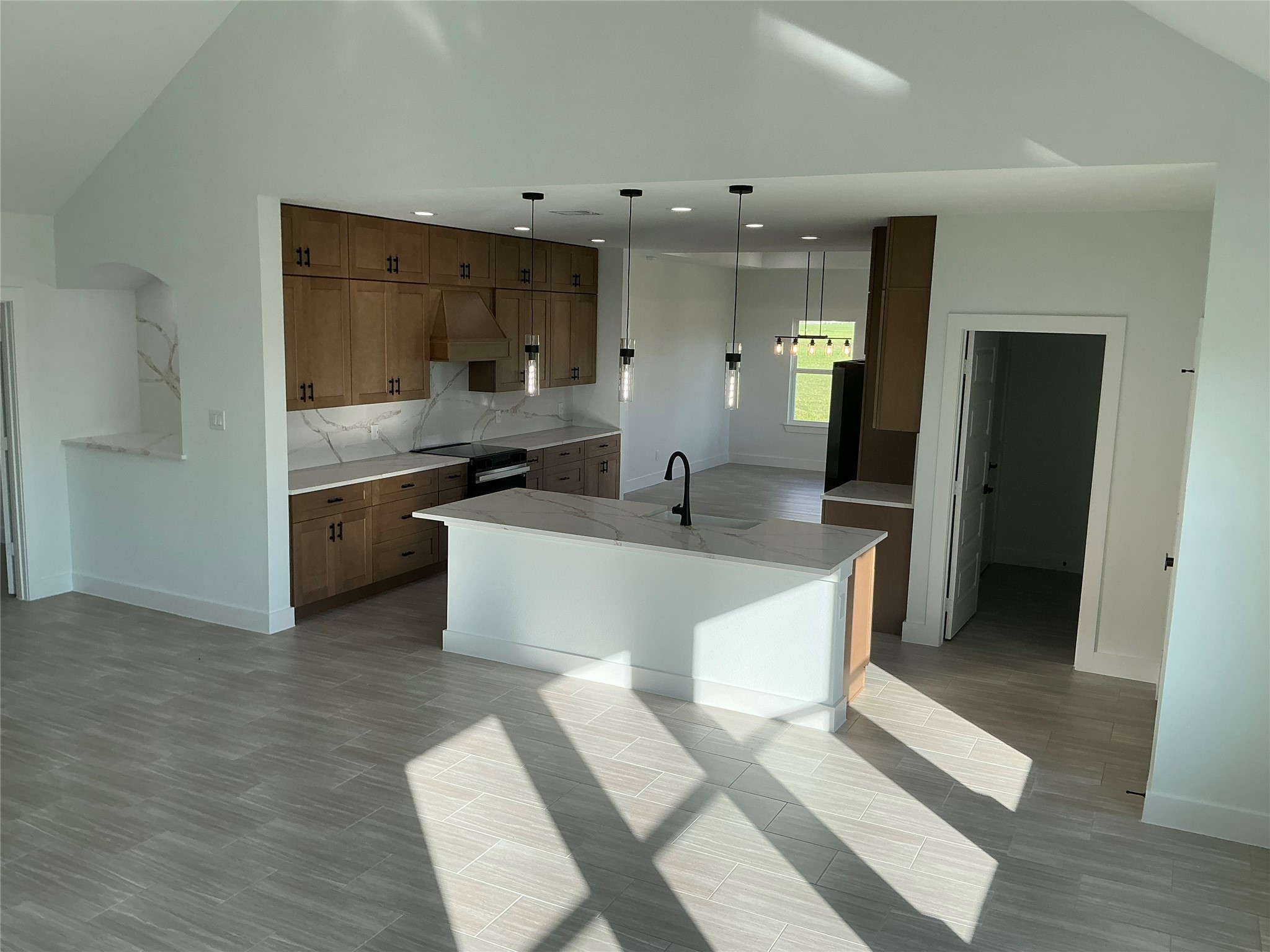 471 Buffalo Trail Angleton, TX 77515 - Photo 10 of 35 This modern kitchen features sleek wooden cabinets, a large island with a sink, and elegant pendant lighting. Bright natural light floods the space, highlighting the flooring and providing a fresh, airy feel.