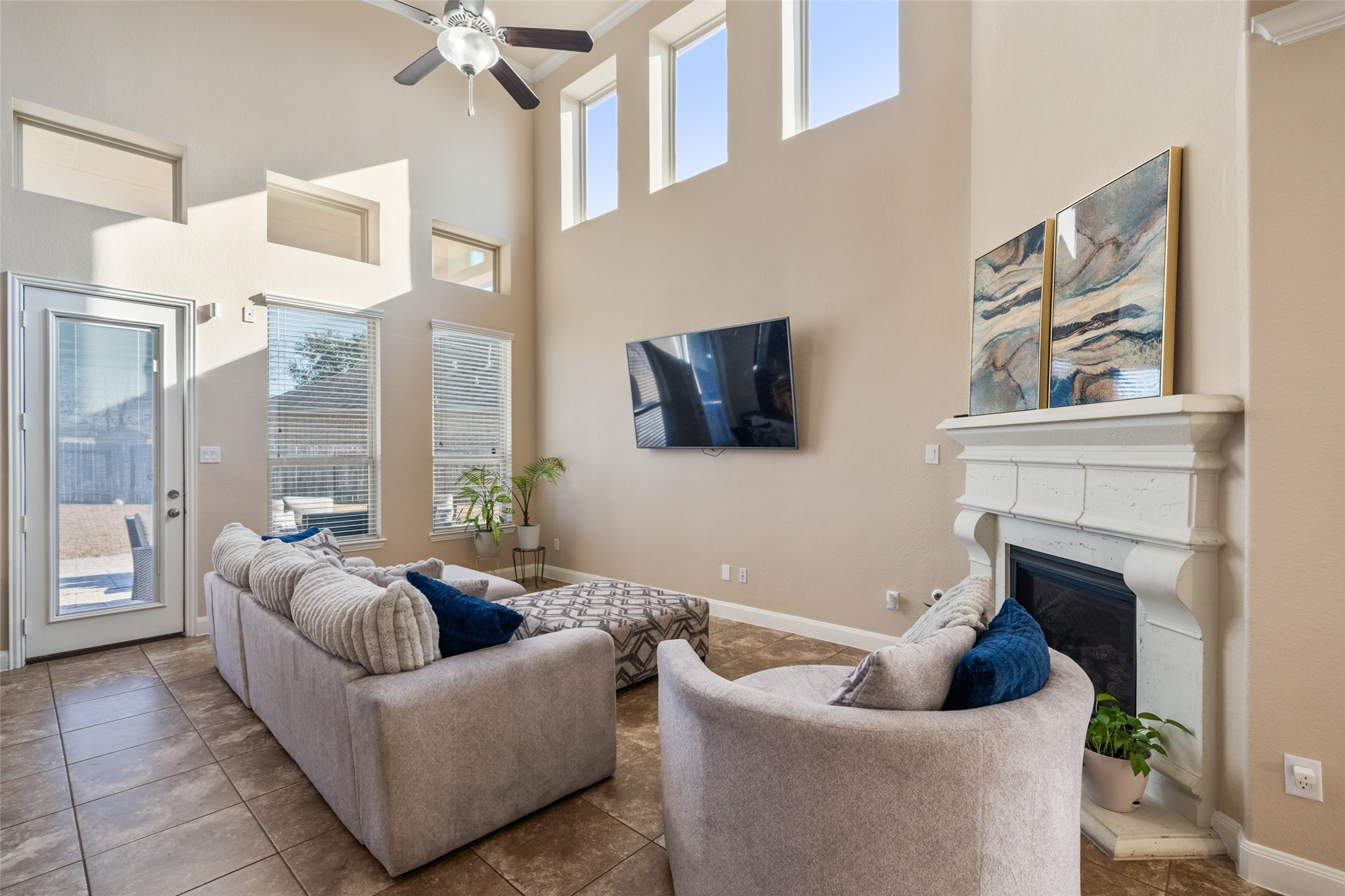 4747 Abercorn Street Rosharon, TX 77583 - Photo 12 of 46 This spacious living room features high ceilings and abundant natural light from large windows. It includes a modern fireplace, a mounted TV, and stylish, comfortable seating. The neutral tones and tile flooring create a warm, inviting atmosphere.