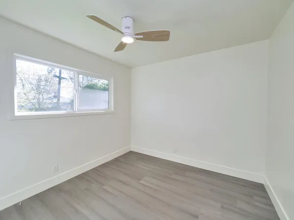 an empty room with wooden floor fan and windows
