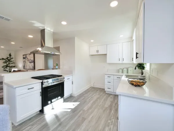 a kitchen with stainless steel appliances a stove a sink dishwasher and white cabinets with wooden floor