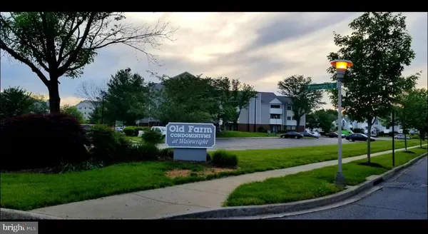 a view of a sign in front of a big yard with plants and large trees