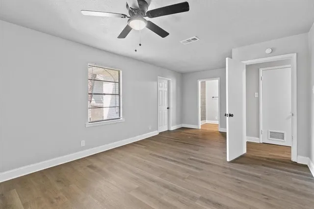 an empty room with wooden floor chandelier fan and windows