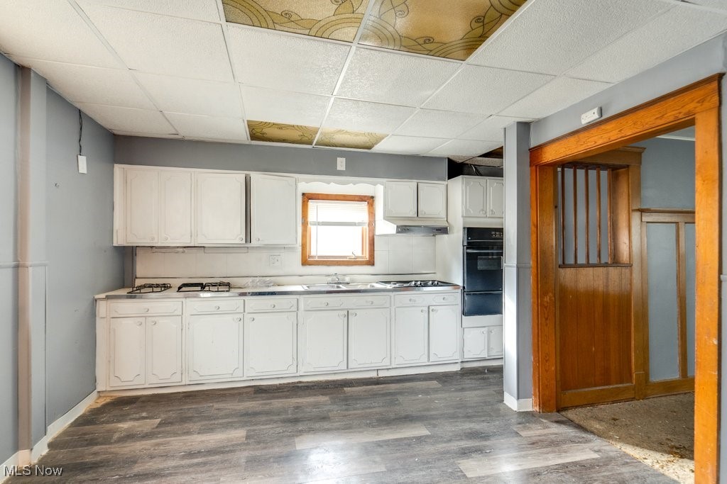 13702 Rugby Road Cleveland, OH 44110 - Photo 6 of 22 Kitchen featuring dark hardwood / wood-style floors, a paneled ceiling, stainless steel gas stovetop, black oven, and white cabinets