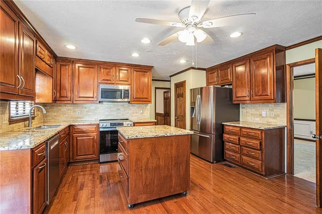 a kitchen with stainless steel appliances granite countertop wooden cabinets a refrigerator a stove a sink and dishwasher with wooden floor