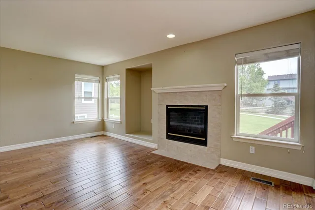 a view of an empty room with wooden floor fireplace and a window