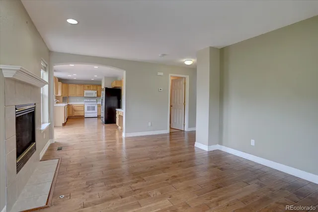 an empty room with wooden floor and a kitchen