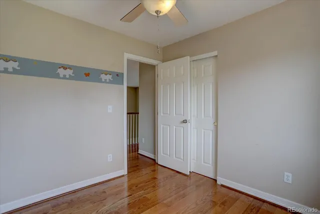 a view of an empty room with wooden floor and a chandelier fan