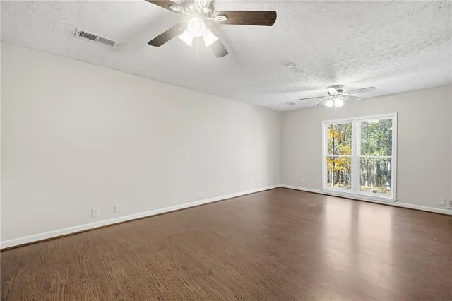 an empty room with wooden floor fan and windows