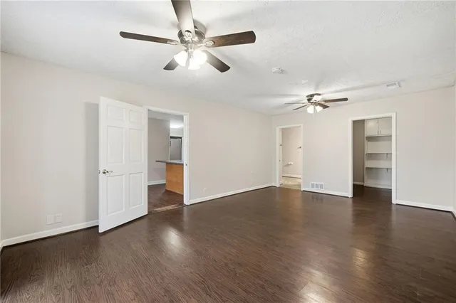 a view of an empty room with wooden floor and a ceiling fan