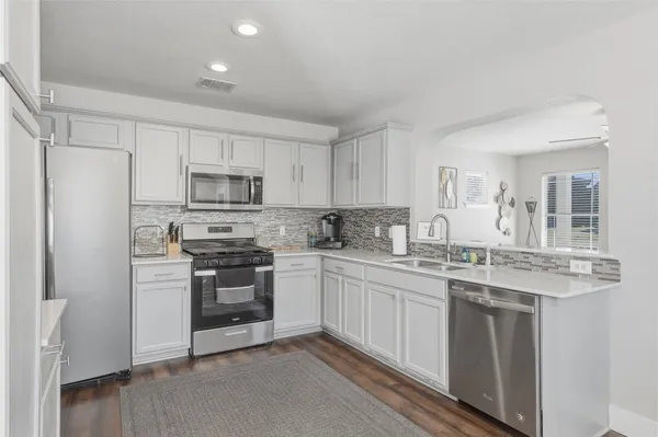 a kitchen with stainless steel appliances granite countertop a stove top oven a sink and white cabinets
