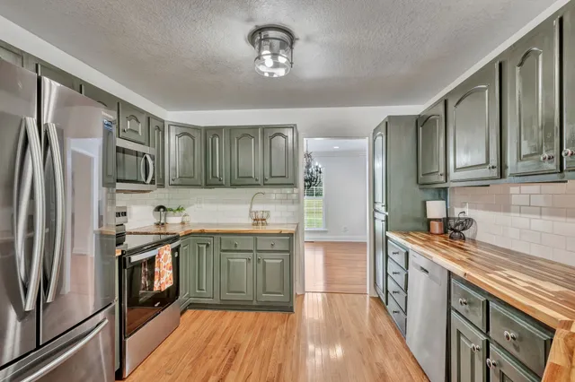 a kitchen with stainless steel appliances granite countertop a refrigerator a sink dishwasher a stove and white countertops with wooden floor