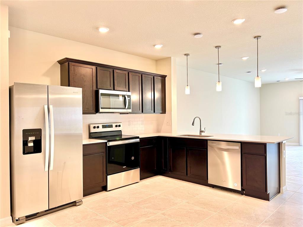 4652 Sparkling Shell Avenue Kissimmee, FL 34746 - Photo 4 of 35 a large kitchen with stainless steel appliances kitchen island granite countertop a refrigerator and a sink