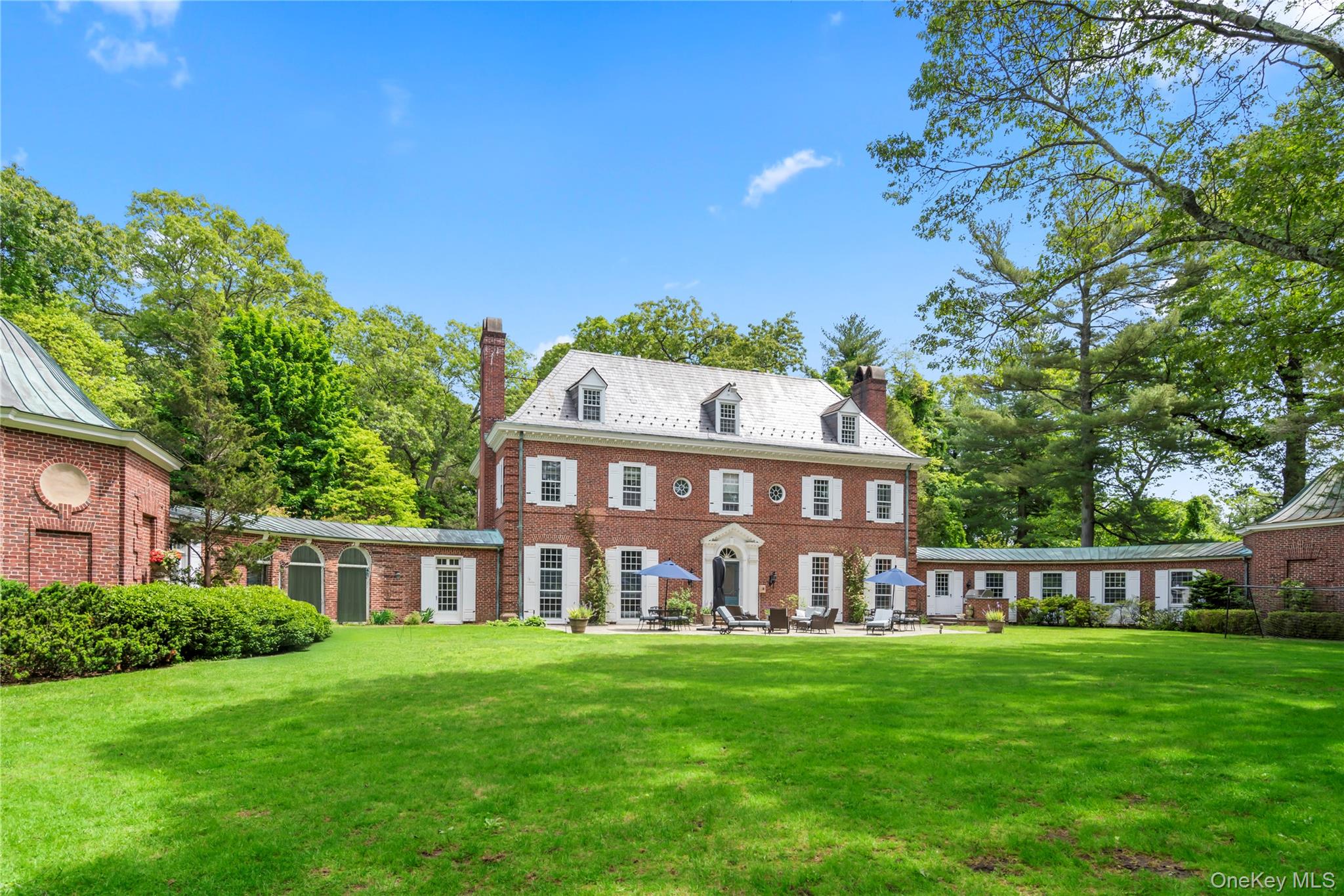 Georgian-style home featuring a chimney, brick siding, a front yard, and a high end roof