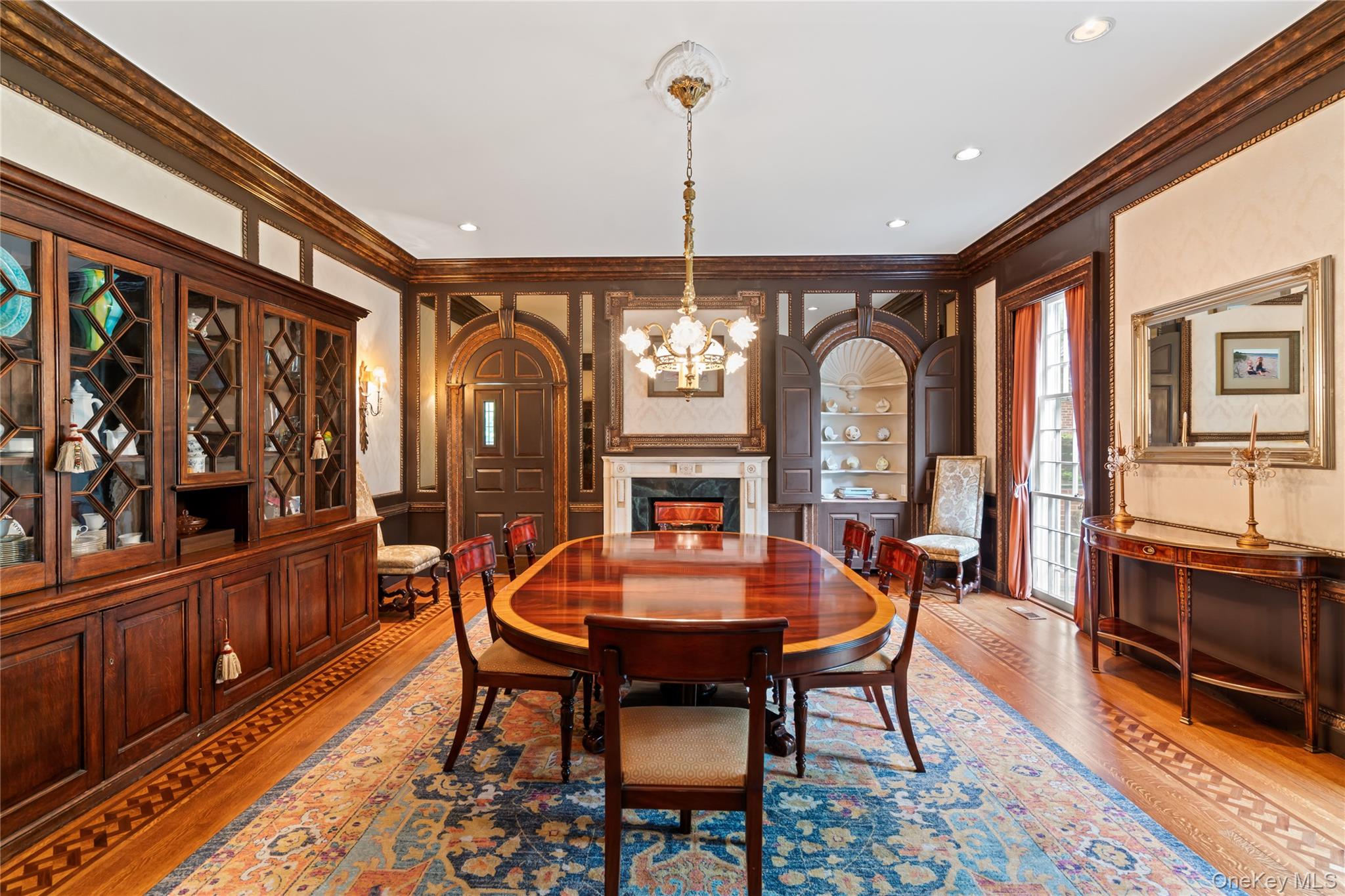 88 Wheatley Road Old Westbury, NY 11568 - Photo 15 of 40 Dining room featuring crown molding, wood finished floors, a chandelier, a decorative wall, and a premium fireplace