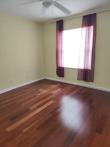 an empty room with wooden floor and windows with curtains