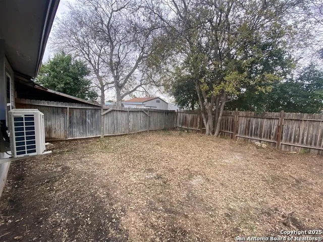 a view of a backyard with large trees and wooden fence