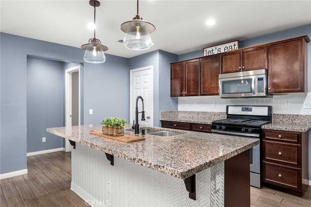 136 Yosemite Avenue Perris, CA 92570 - Photo 4 of 31 a kitchen with stainless steel appliances granite countertop wooden cabinets a microwave a stove and a center island