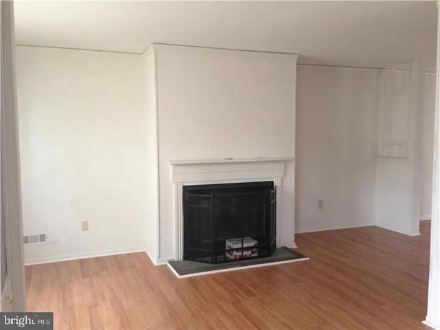 a view of an empty room with wooden floor and a fireplace