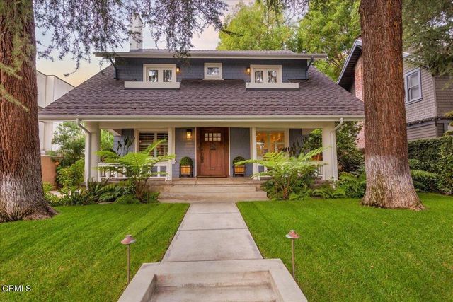 a view of a brick house with a yard garden and a large tree