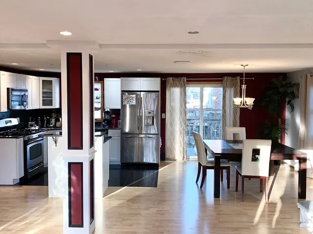 a kitchen with stainless steel appliances kitchen island granite countertop a refrigerator a stove a dining table and chairs with wooden floor