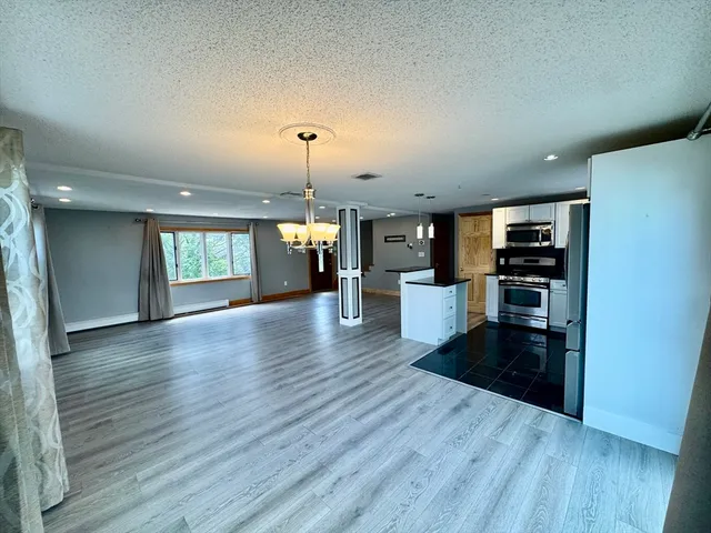 an empty room with wooden floor and kitchen view