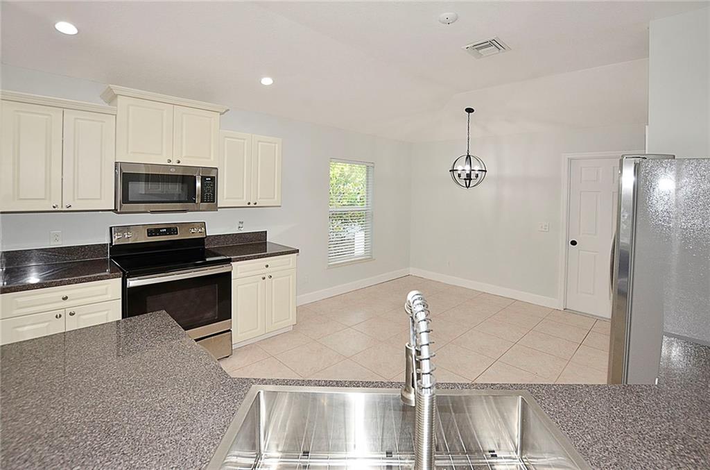 3285 3rd Place Vero Beach, FL 32968 - Photo 14 of 34 a kitchen with stainless steel appliances kitchen island granite countertop a stove a sink and a microwave