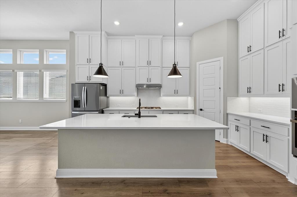 2237 Pika Road Northlake, TX 76247 - Photo 9 of 37 Modern kitchen featuring a large center island with a sink and pendant lighting, extensive white cabinetry with dark hardware, stainless steel appliances, and wood-finish flooring