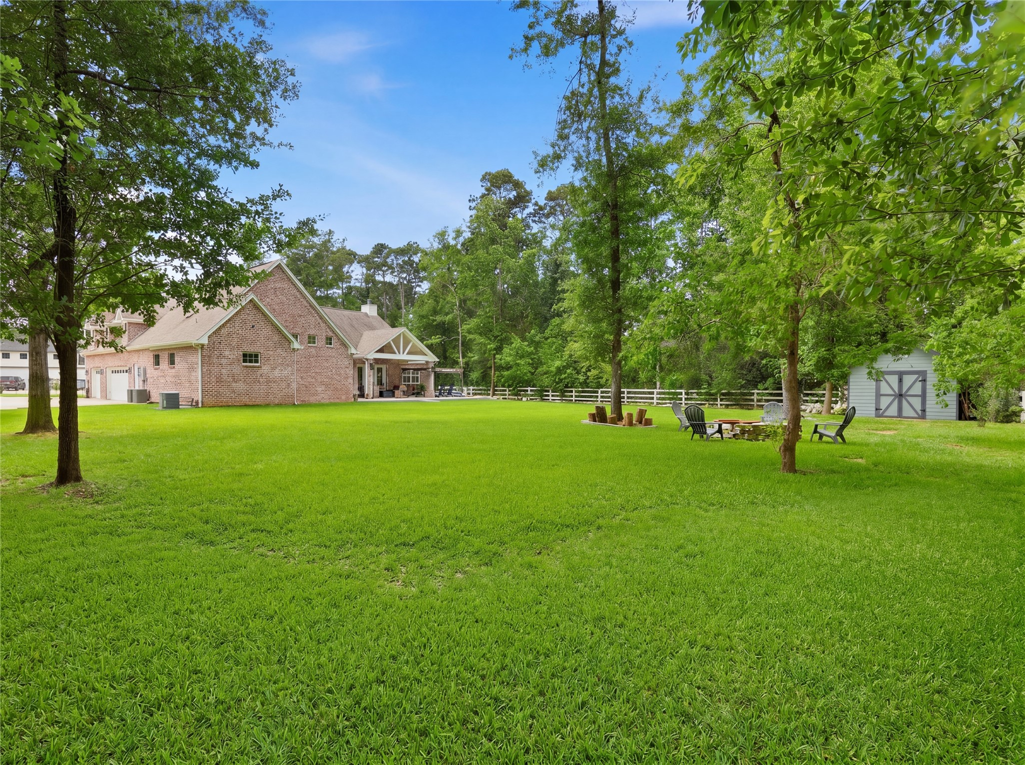 7106 Hampton Court Spring, TX 77389 - Photo 26 of 31 Spacious backyard with lush green grass, surrounded by mature trees. There's a huge storage shed and a cozy seating area with a fire pit on the other, perfect for outdoor gatherings.
