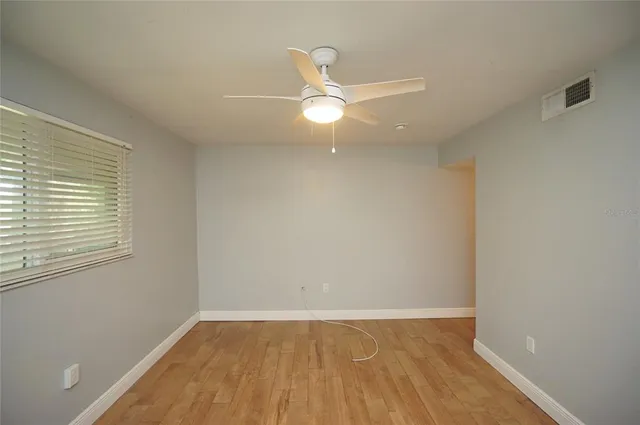 an empty room with wooden floor fan and windows