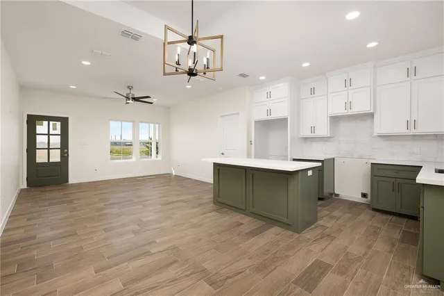a large kitchen with stainless steel appliances granite countertop a stove a sink dishwasher a refrigerator and white cabinets with wooden floor