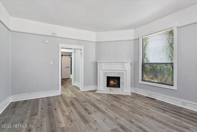 a view of an empty room with wooden floor fireplace and a window