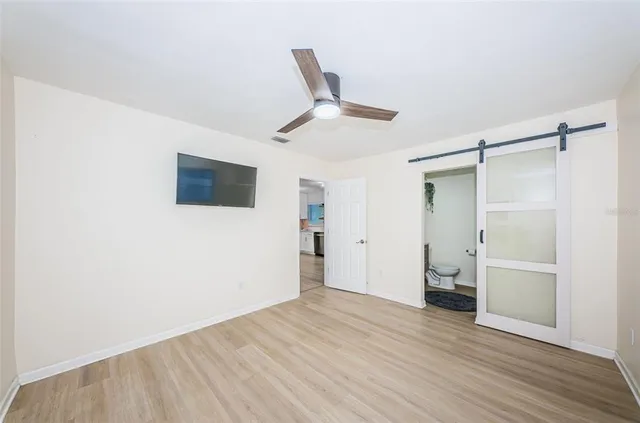 a view of an empty room with wooden floor and a ceiling fan