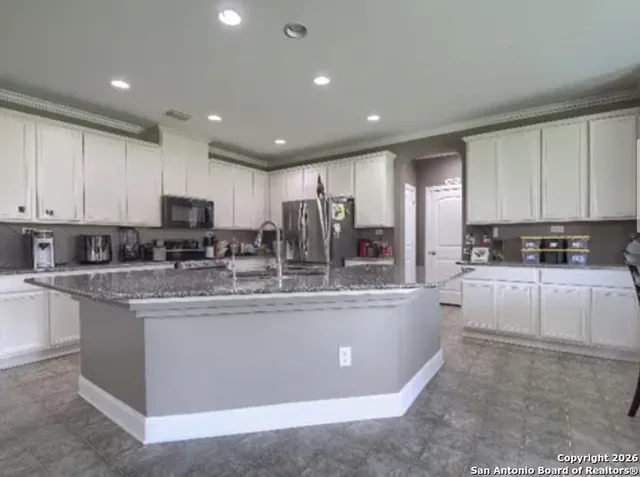 a large kitchen with stainless steel appliances granite countertop a stove a sink a refrigerator and white cabinets