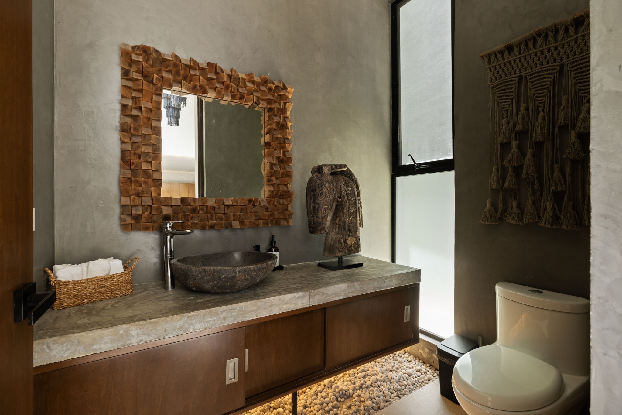 6 Country Club, Unit 4 Nome, TX 77629 - Photo 15 of 45 This exquisitely designed first-floor half-bath offers resort-style convenience for guests by seamlessly blending raw organic textures with sleek contemporary luxury. At the center of the space, a hand-carved natural stone basin sits atop a thick concrete vanity countertop equipped with a premium chrome faucet. Anchoring the entire vanity area, a striking, multi-dimensional mosaic wood-block mirror frame introduces rich warmth and sculptural texture.