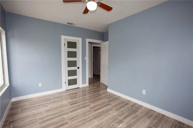 an empty room with wooden floor chandelier fan and windows