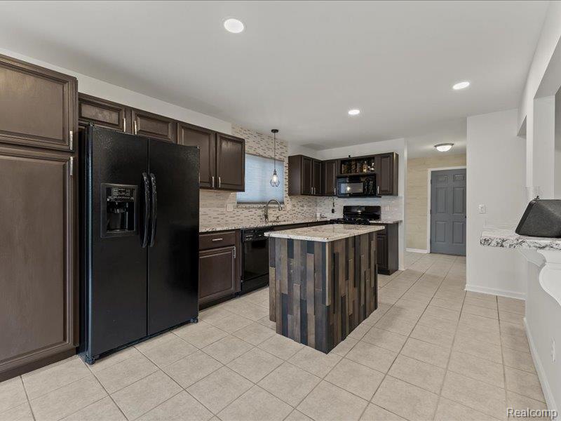 29213 Rachid Lane New Baltimore, MI 48047 - Photo 7 of 26 Kitchen featuring dark wood finish cabinetry, black appliances, decorative backsplash, light tile patterned floors, and a kitchen island
