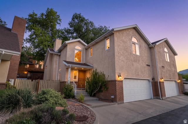 Stucco exterior featuring arched windows, brick accents, multiple garage doors, and mature landscaping