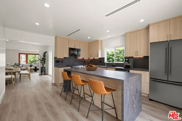 a kitchen with stainless steel appliances granite countertop a refrigerator a stove a sink a dining table and chairs with wooden floor