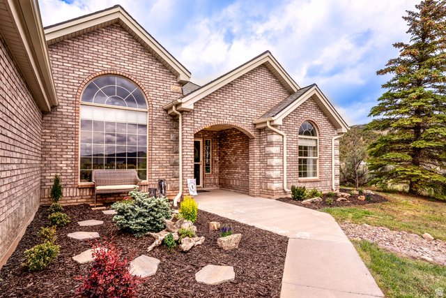 7343 North Sawtooth Cv Road Vernal, UT 84078 - Photo 3 of 64 Brick exterior featuring an arched transom window, a prominent entry archway, a concrete pathway, landscaped garden beds with decorative rocks and mulch, and a mature evergreen tree