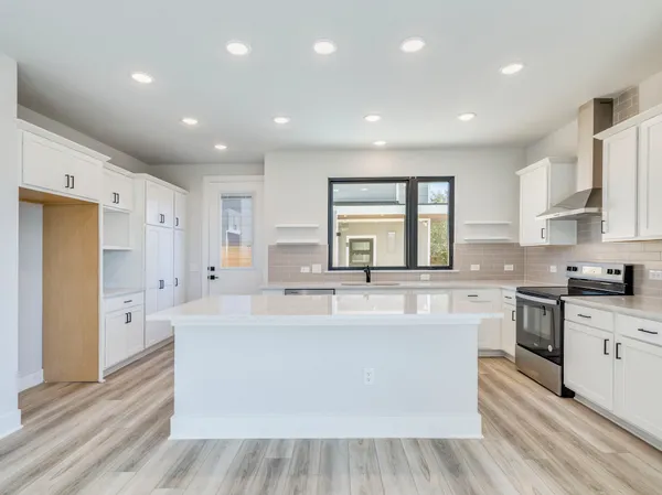 a large white kitchen with stainless steel appliances granite countertop a stove a sink dishwasher and a refrigerator with wooden floor