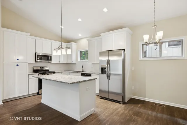 a kitchen with stainless steel appliances granite countertop a refrigerator a sink dishwasher a stove and white cabinets with wooden floor