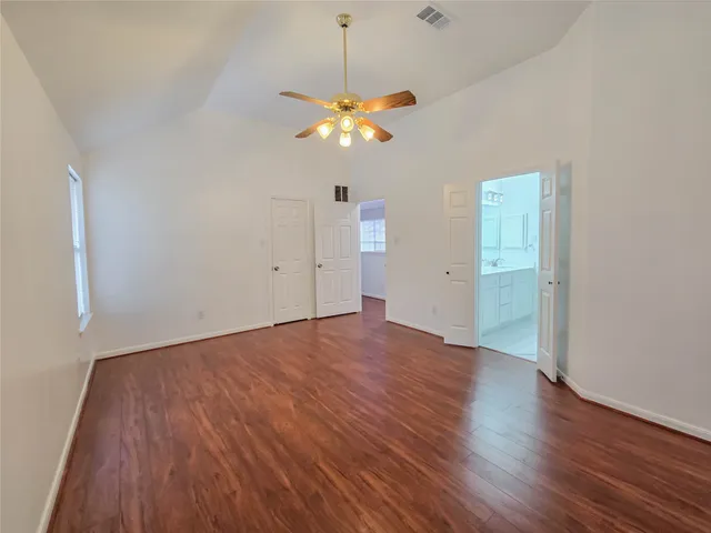 an empty room with wooden floor chandelier fan and windows