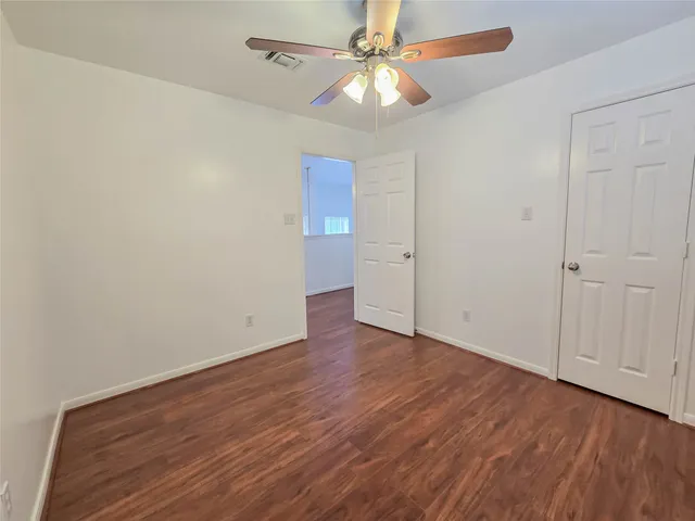 an empty room with wooden floor fan and windows