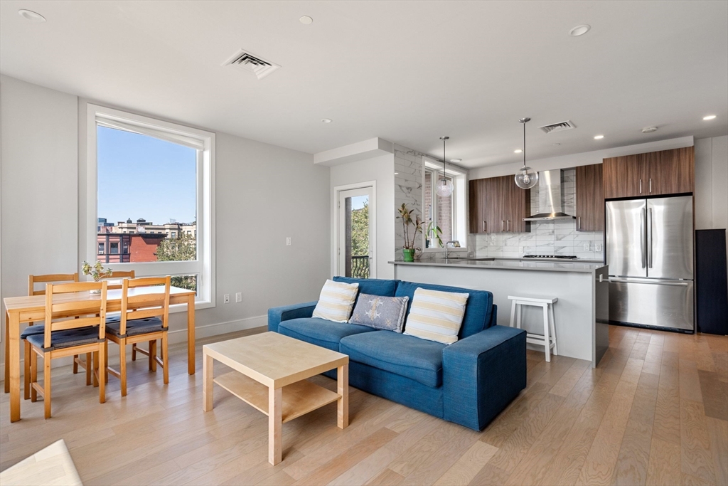 44-50 Symphony Road, Unit 403 Boston, MA 02115 - Photo 3 of 28 a living room with stainless steel appliances kitchen island granite countertop a refrigerator a stove a sink dishwasher and a dining table with wooden floor