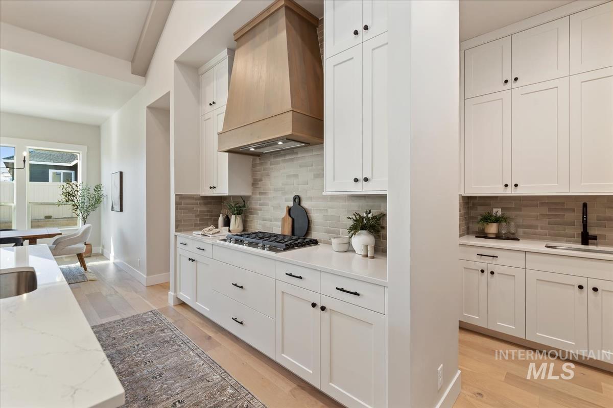 7355 Powell Place Eagle, ID 83714 - Photo 11 of 37 Modern kitchen featuring white cabinetry, light wood-finish flooring, a wood-finish range hood, light-toned brick-patterned backsplash, and quartz countertops