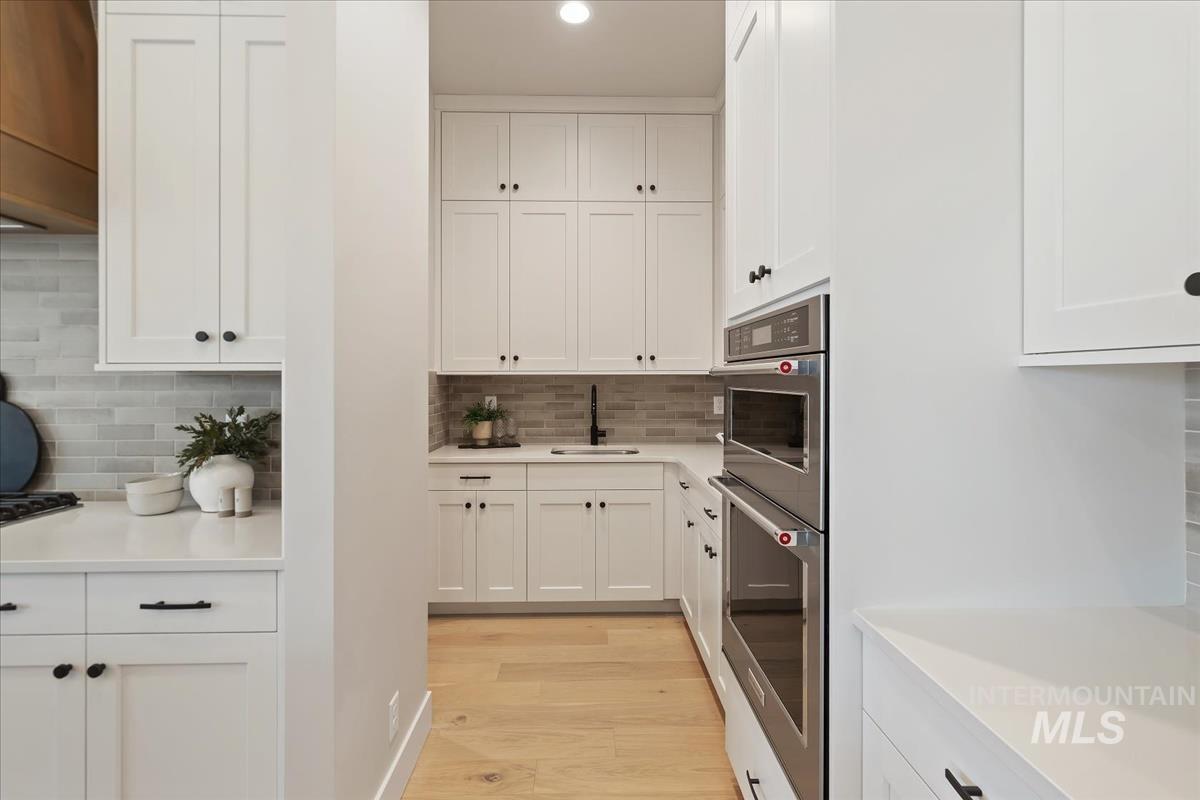 7355 Powell Place Eagle, ID 83714 - Photo 12 of 37 Kitchen featuring white shaker-style cabinetry, light wood-finish flooring, stainless steel double wall ovens, a grey subway tile backsplash, and light-toned countertops