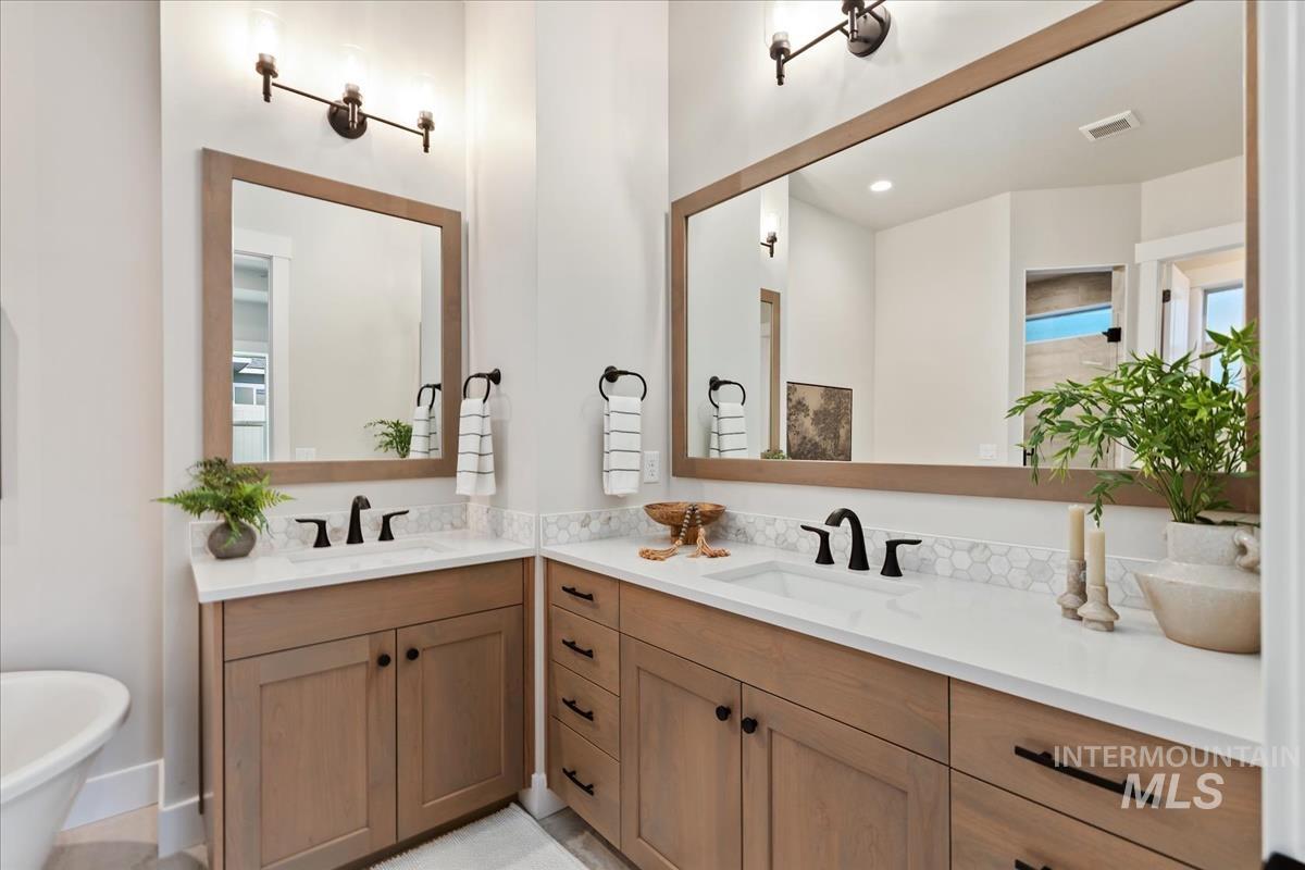 7355 Powell Place Eagle, ID 83714 - Photo 18 of 37 Dual vanity bathroom featuring light wood-finish cabinetry, white countertops, hexagon tile backsplash, and matte black fixtures