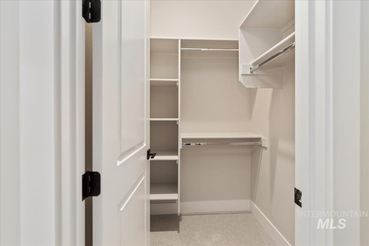 7355 Powell Place Eagle, ID 83714 - Photo 29 of 37 Walk-in closet featuring white built-in shelving, multiple hanging rods, and light-toned carpet flooring