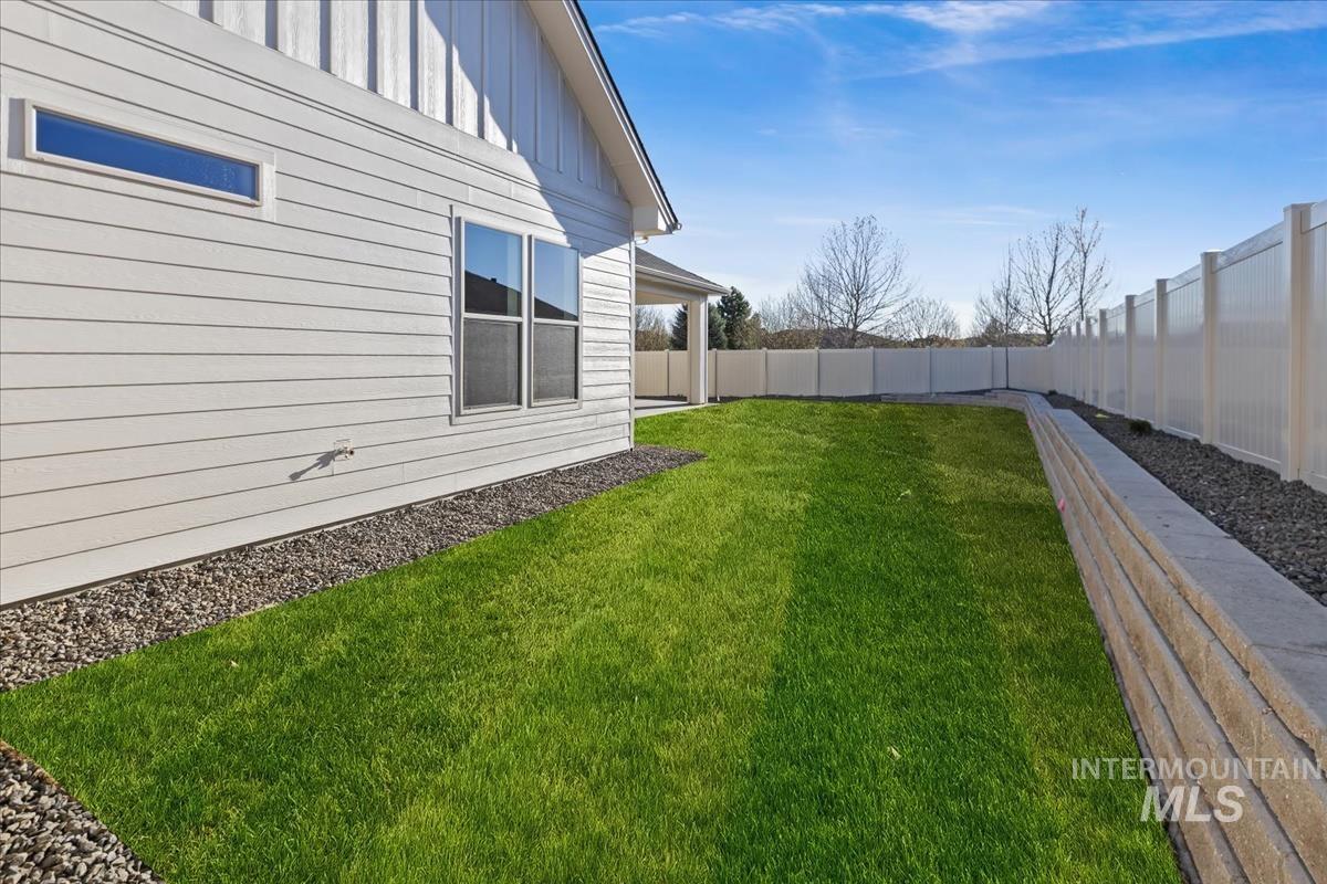 7355 Powell Place Eagle, ID 83714 - Photo 36 of 37 Fenced backyard featuring a manicured lawn, a retaining wall, and a rock border along the house foundation