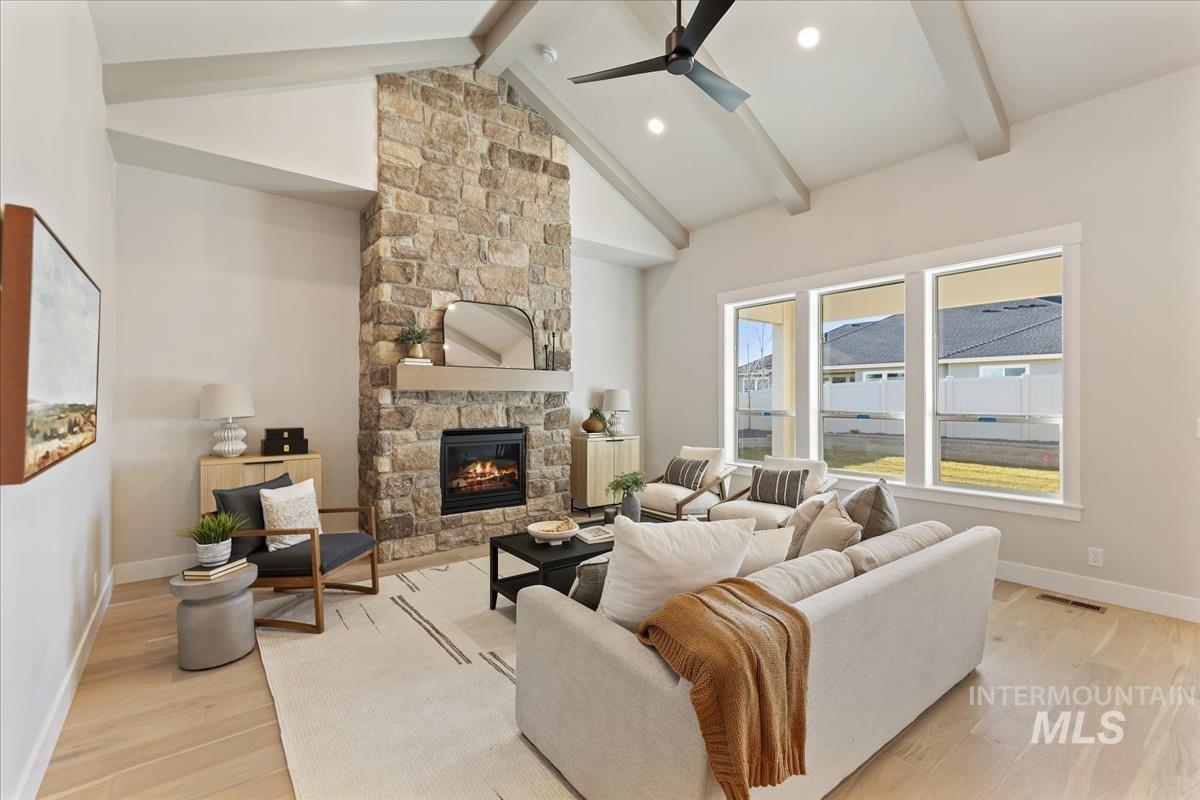 7355 Powell Place Eagle, ID 83714 - Photo 4 of 37 Spacious living area featuring a vaulted ceiling with exposed beams, stone fireplace, light wood-finish flooring, and large windows